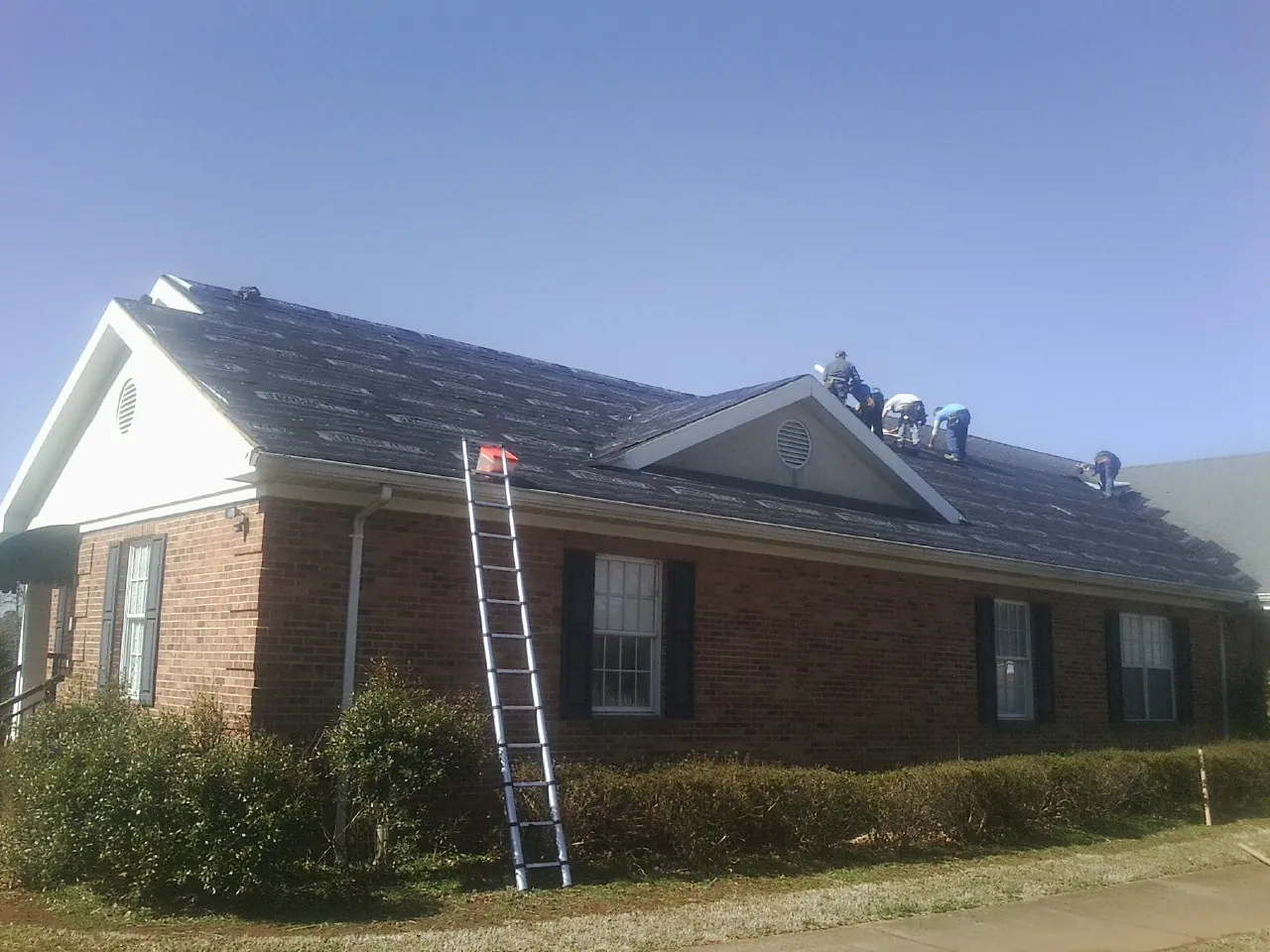 Crew tearing shingles off a brick ranch roof with a ladder set — Metal Roof Repair work by our crew in Wawarsing