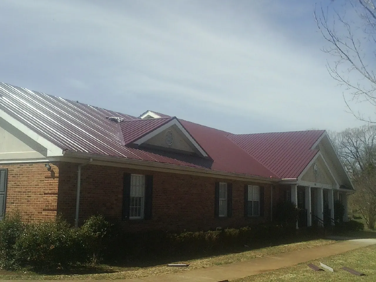 Red metal roof with gabled entries on a long brick building, from a Hail Damage Roof Repair job in Wawarsing