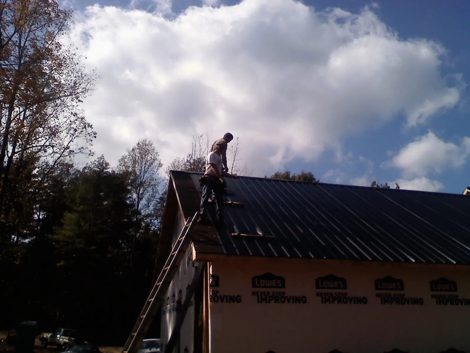 Roofer fastening dark metal panels high against a cloudy sky, from a Roof Inspection job in Wawarsing