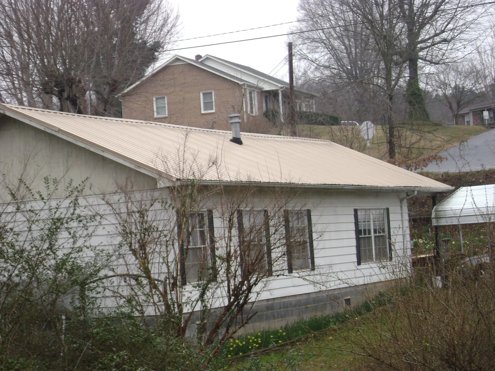Tan metal roof on a white sided house set into a hillside — Commercial Roofing by Roofing Brothers in Wawarsing